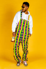 Load image into Gallery viewer, Man in Mardi Gras overalls holding a bottle, wearing sneakers and sunglasses, close-up of shoe and hand with bottle.