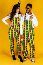 Load image into Gallery viewer, A man and woman in Mardi Gras overalls, ready for a day of celebration with beignets in hand.