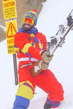 Load image into Gallery viewer, Man in vintage ski suit holding ski and snowboard, embodying 80s nostalgia.
