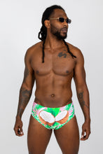 Load image into Gallery viewer, A man in The Pi√±a Colada | Tropical Coconuts Swim Brief and sunglasses, with dreadlocks, sips a Miami Vice cocktail.
